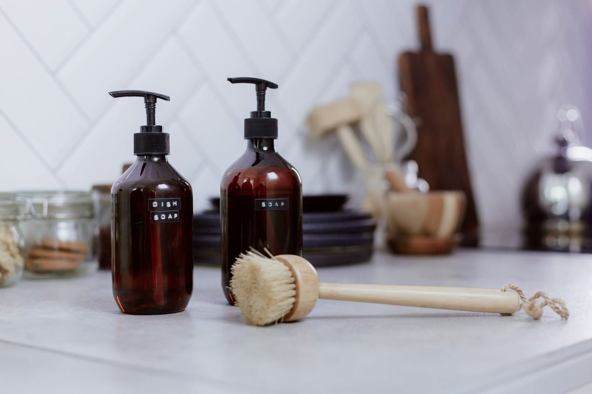 brown glass pump bottles and a wooden dish brush on a white counter