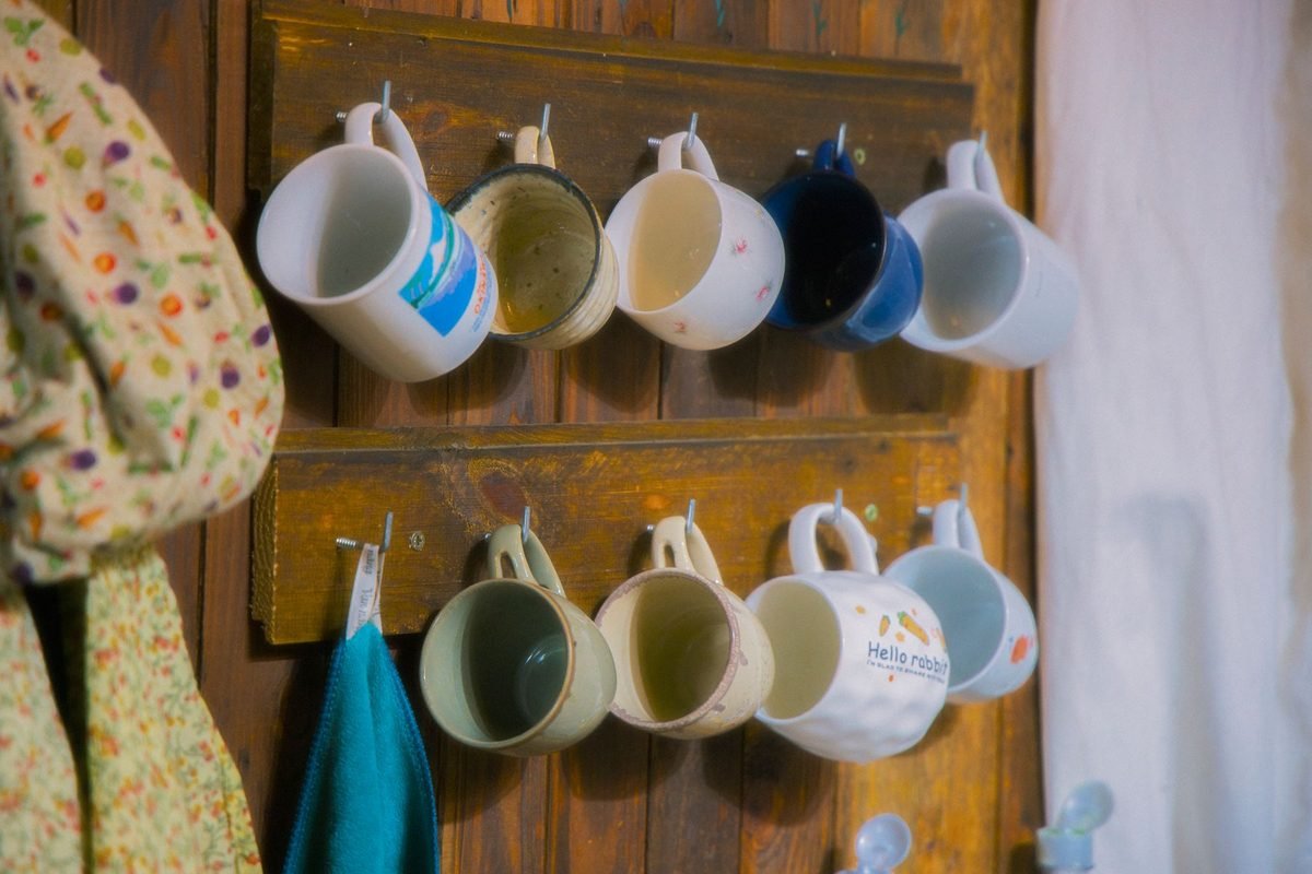 colorful mugs hanging from pegs on a wooden wall rack