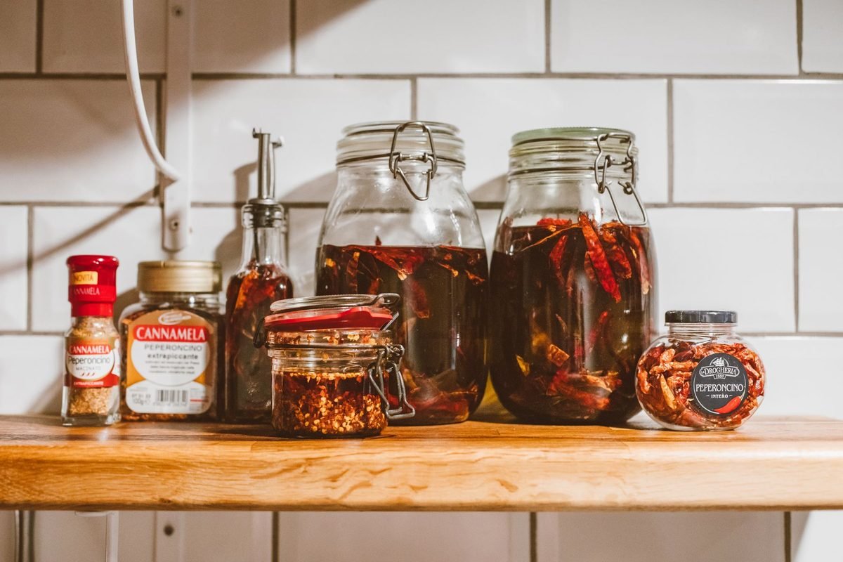 glass jars of sauces, oils and condiments on a wooden counter shelf