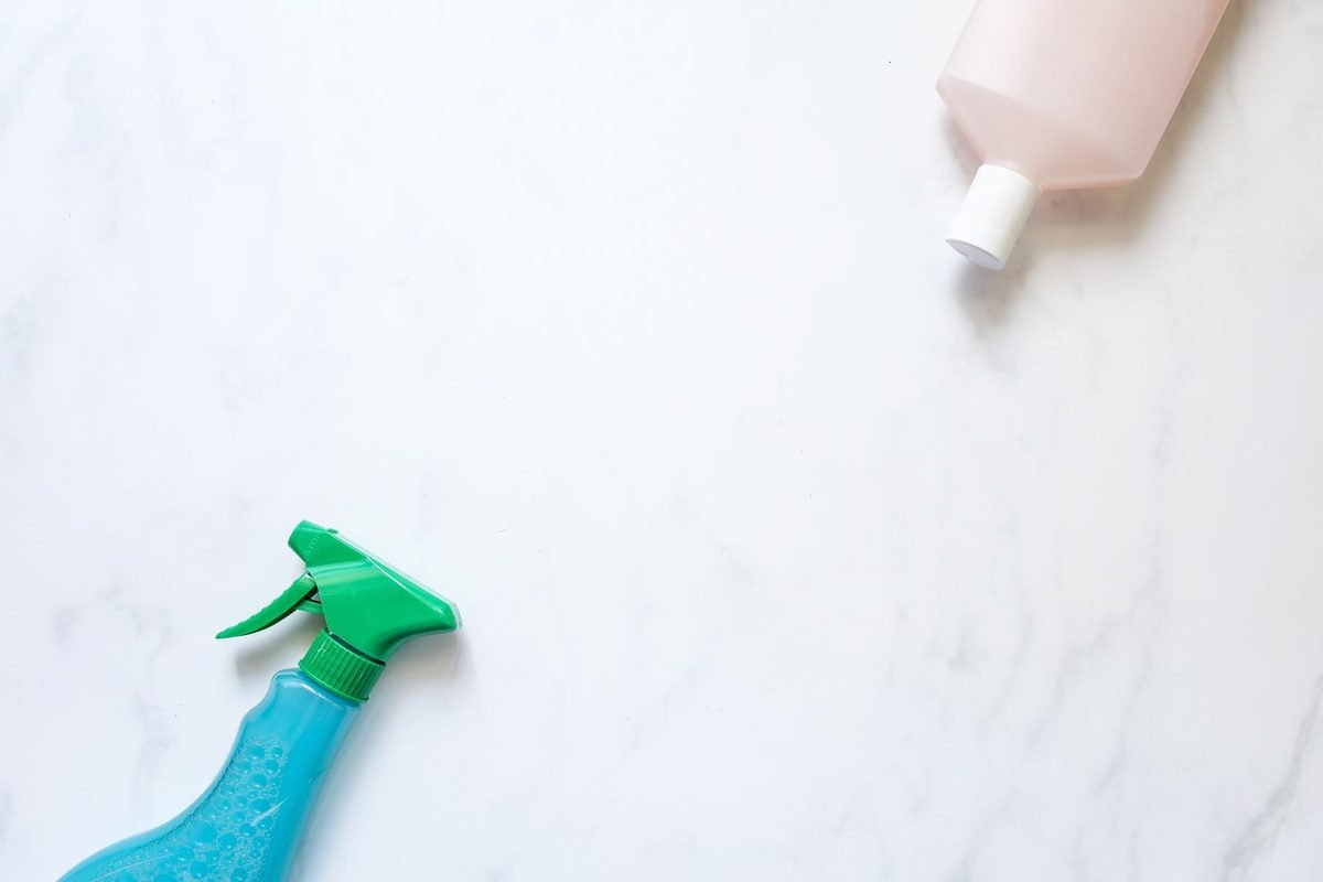 hand spraying a blue cleaning bottle on a white marble bathroom counter