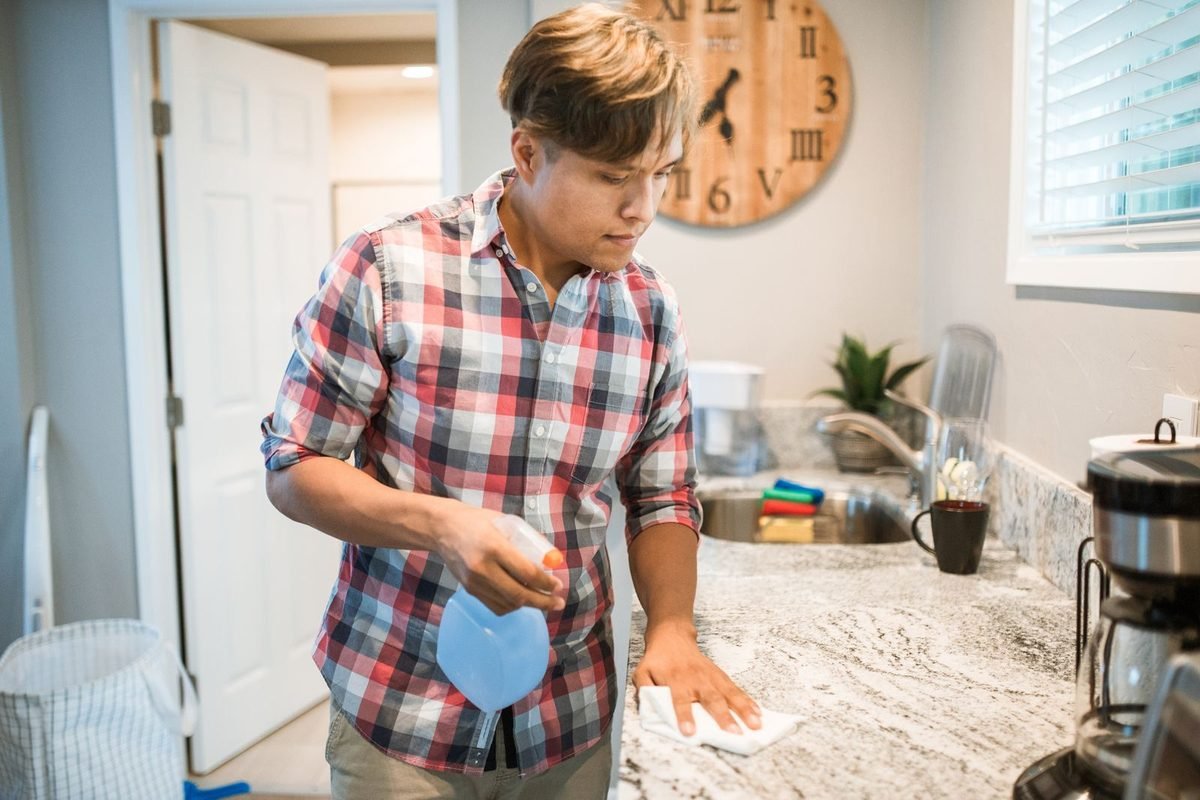 man wiping a kitchen counter with a cleaning spray