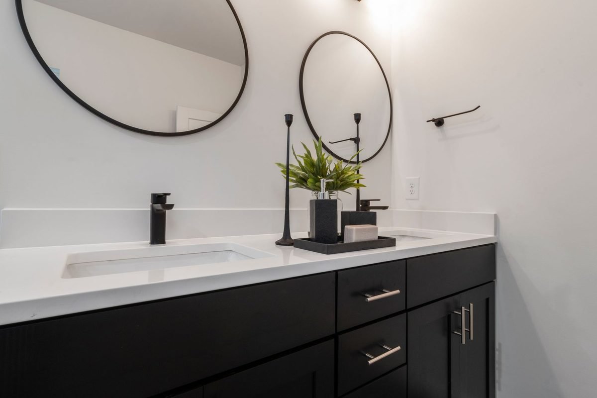 modern bathroom vanity with a black cabinet, round mirror and white counter