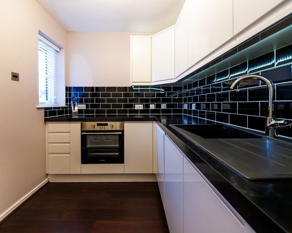 narrow modern kitchen with black tiles, white cabinets and a sink