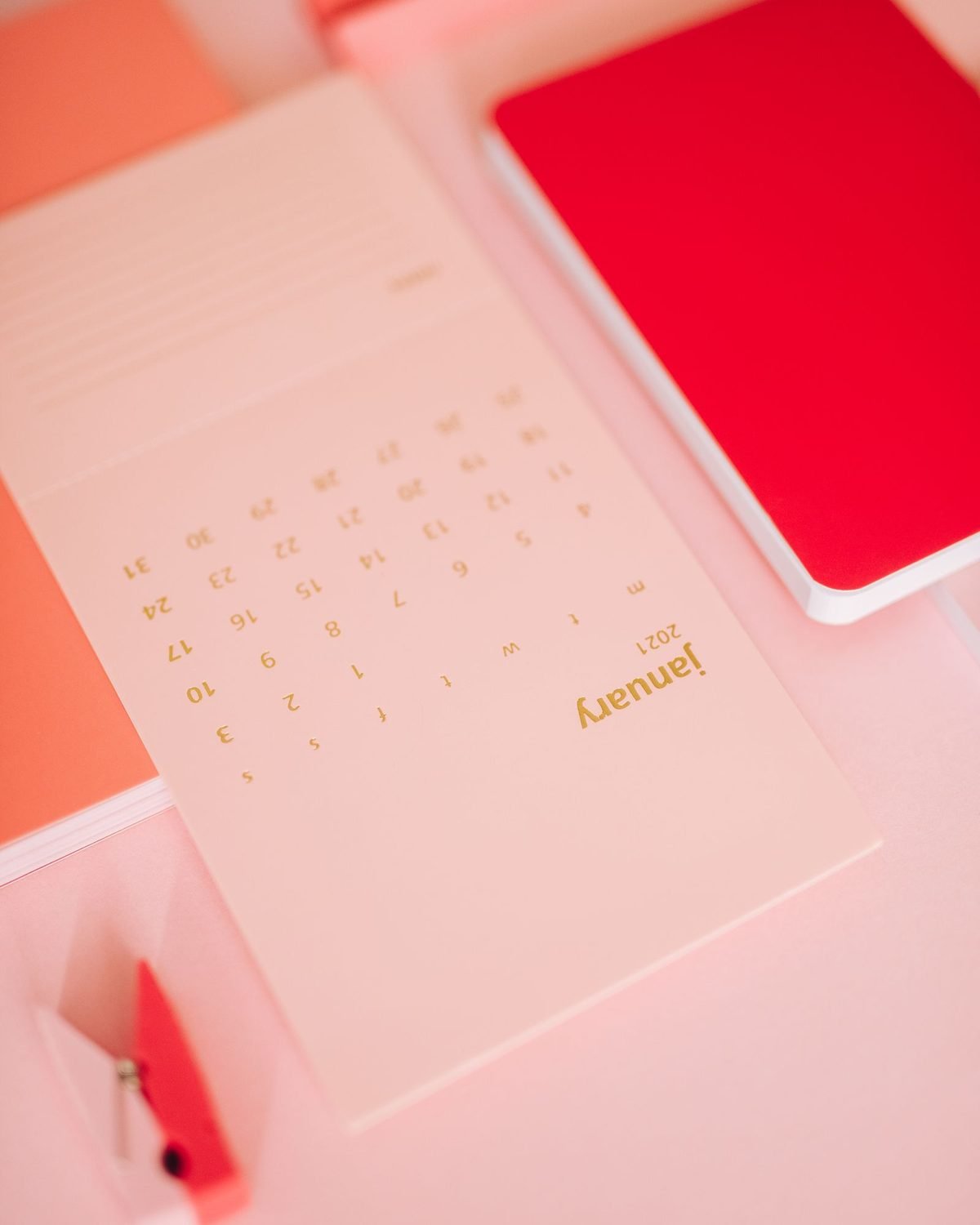 notebooks and a calendar page on a pink desk for tracking a january organization challenge
