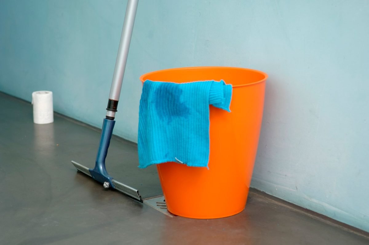 orange bucket with a blue cloth and a mop in a bathroom