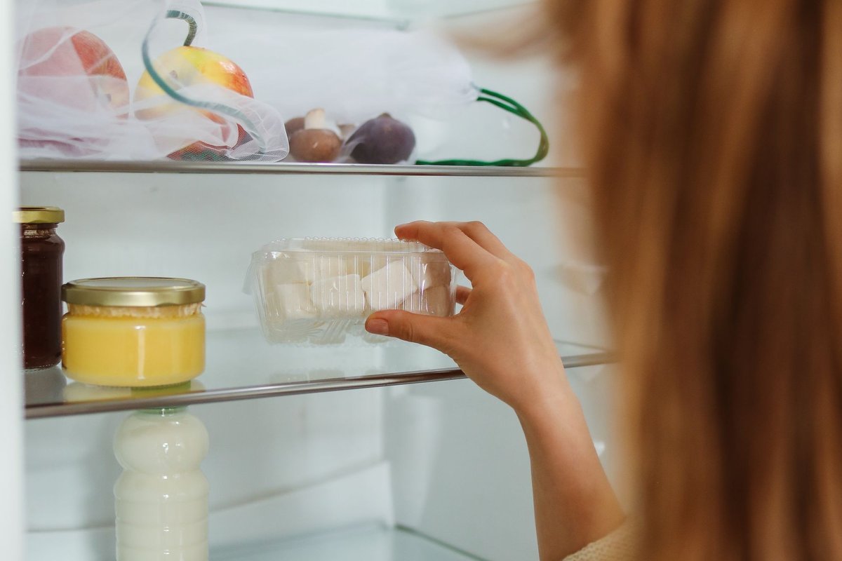Hand reaching for a jar in an organized fridge with storage containers