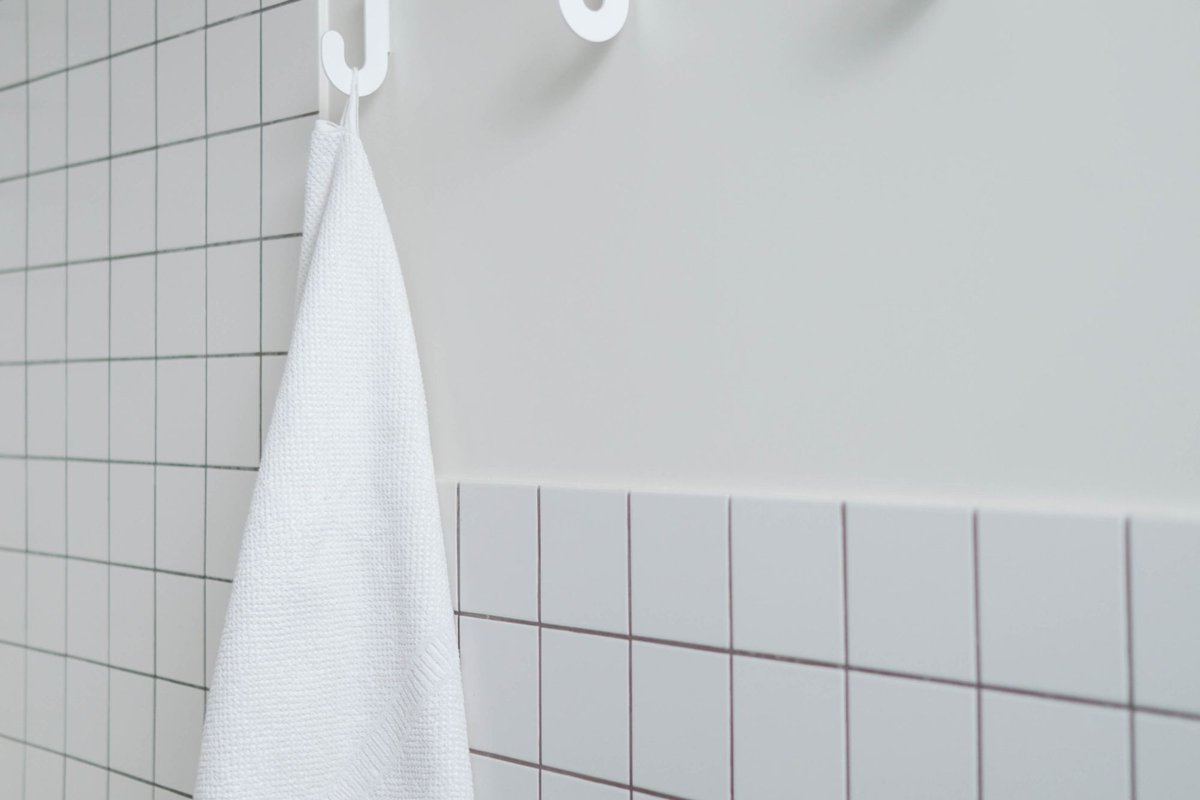 White towel hanging on hooks in a white tiled bathroom