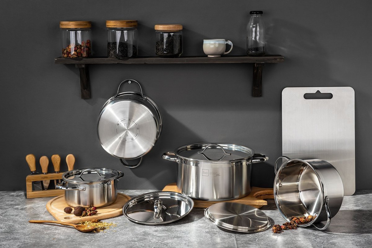 Stainless steel pots with lids stored neatly under a kitchen shelf