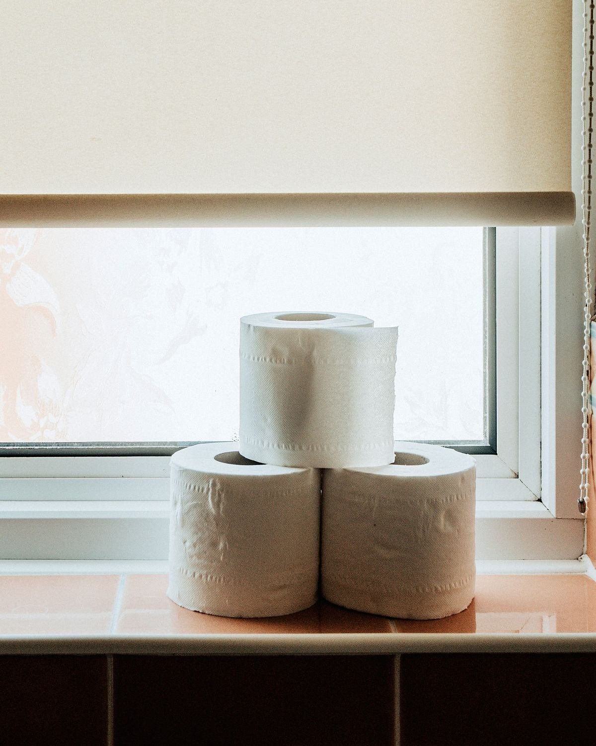 rolls of toilet paper stacked on a bathroom windowsill