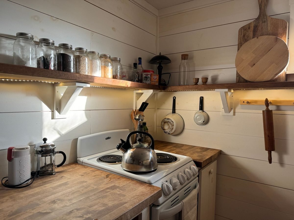 small kitchen with an open shelf above the stove and utensils on a hanging rail