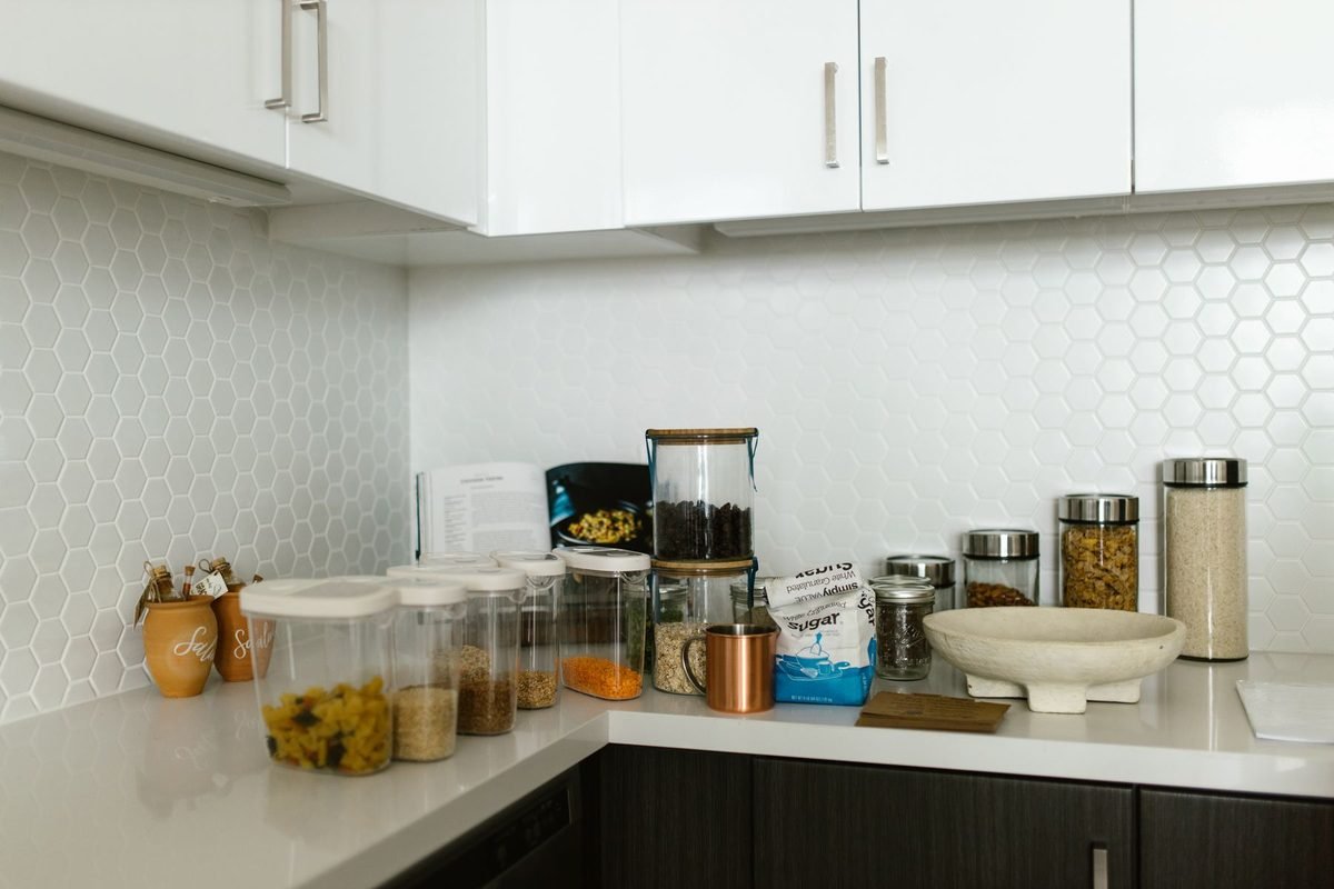 tidy kitchen counter with clear food storage containers and glass jars lined up against a white backsplash