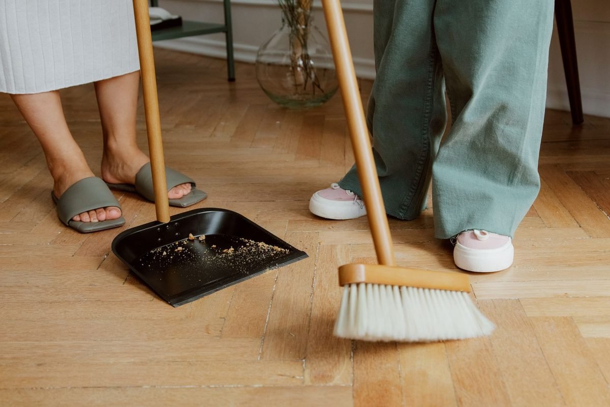 two people sweeping a wooden floor with a broom and dustpan