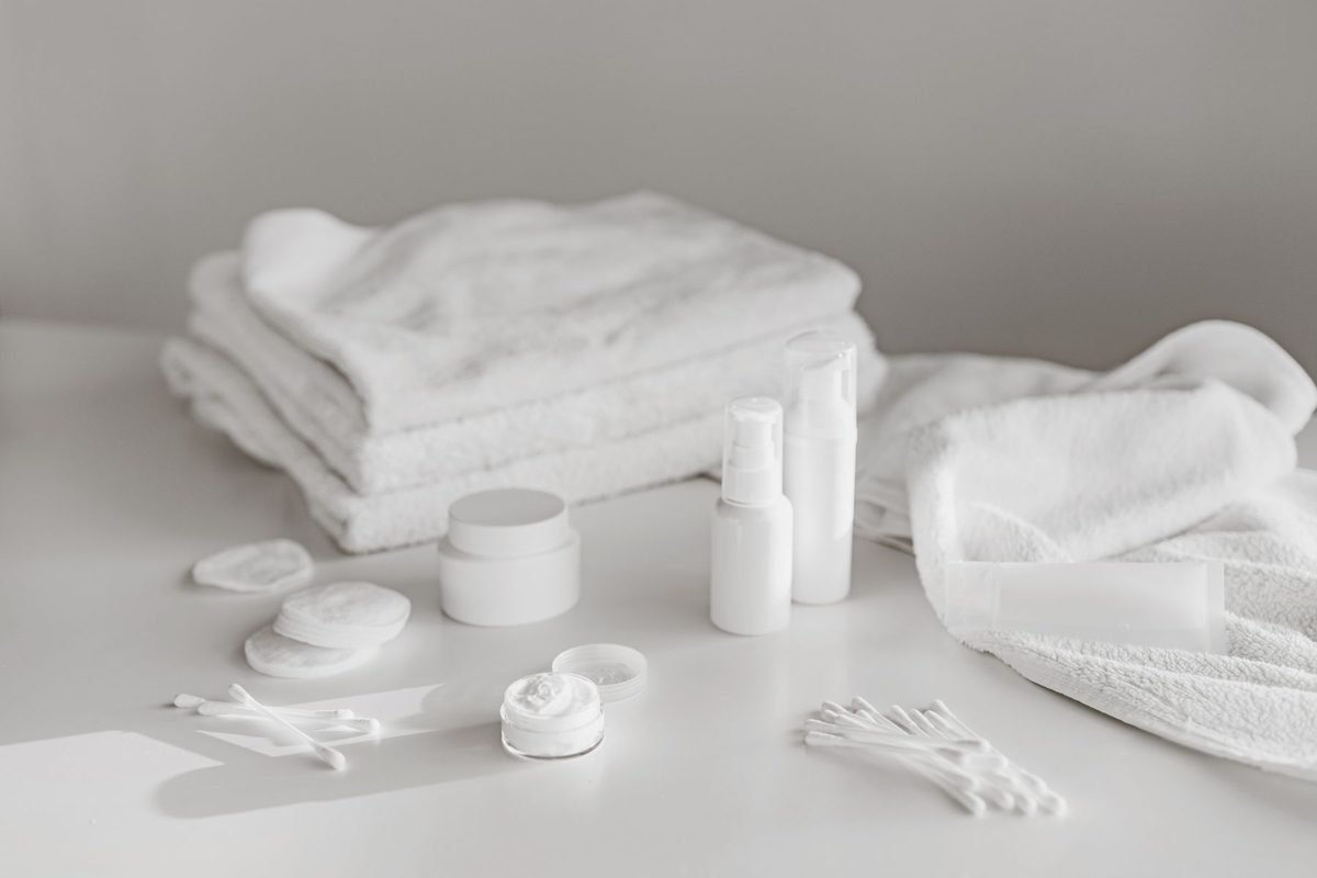 white skincare products, towels and cotton pads on a white surface