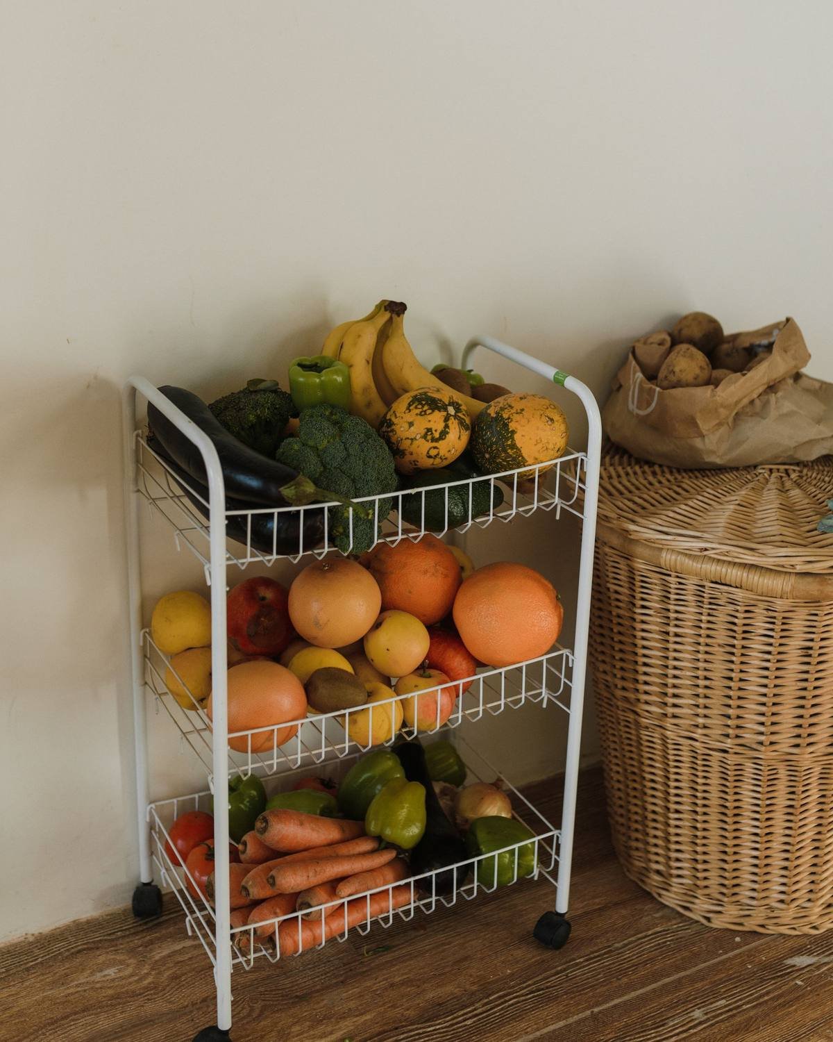 white three-tier rolling cart holding fruits and vegetables in a kitchen