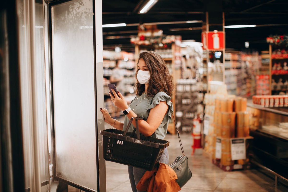 woman checking a shopping list on her phone while shopping with a basket