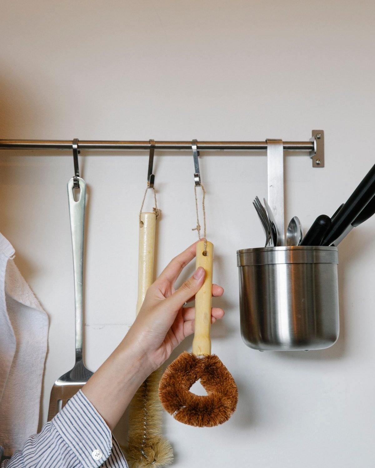 woman hanging a ladle on a wall-mounted kitchen rail with hooks