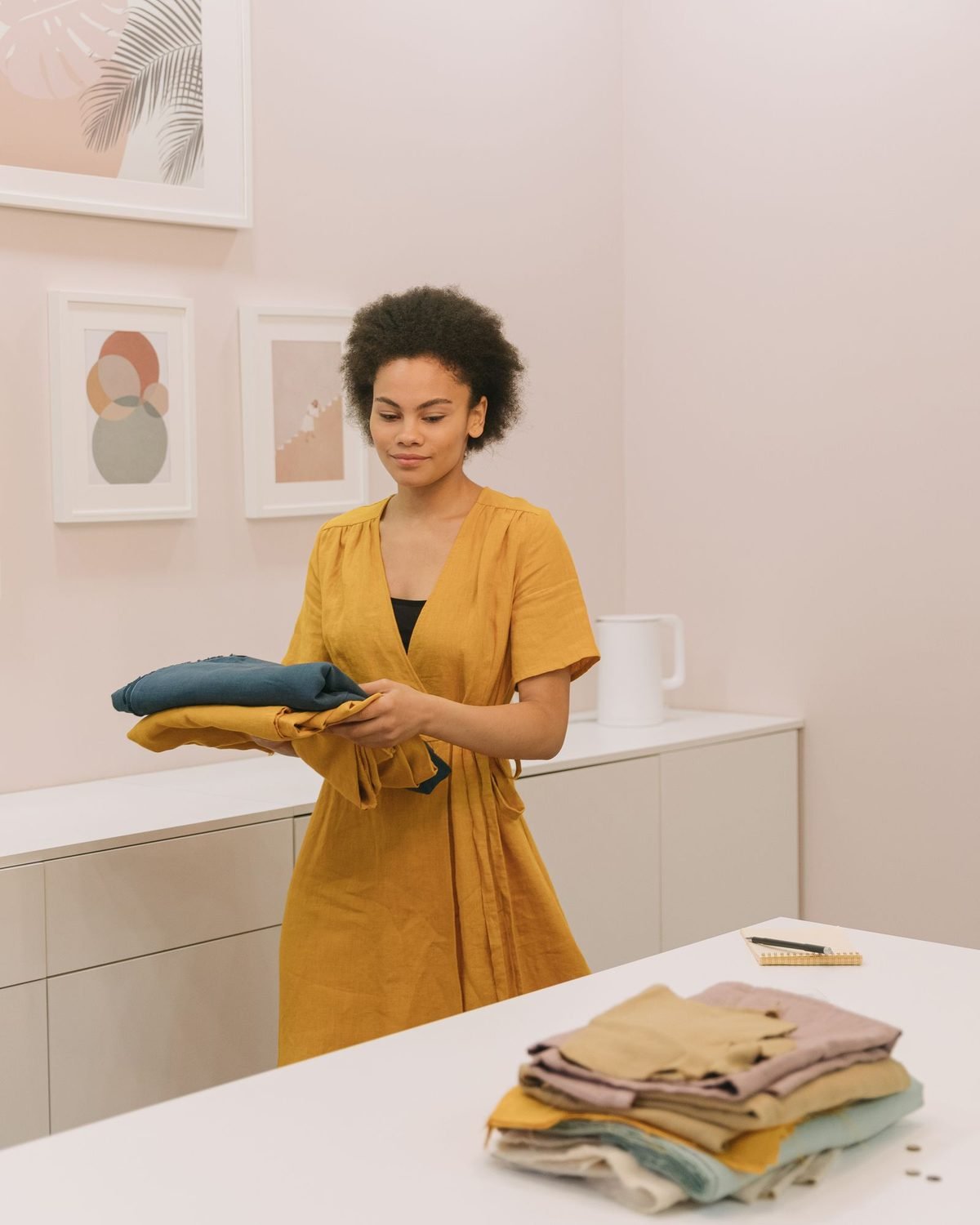 woman in a yellow dress holding a stack of folded clothes in a bright room