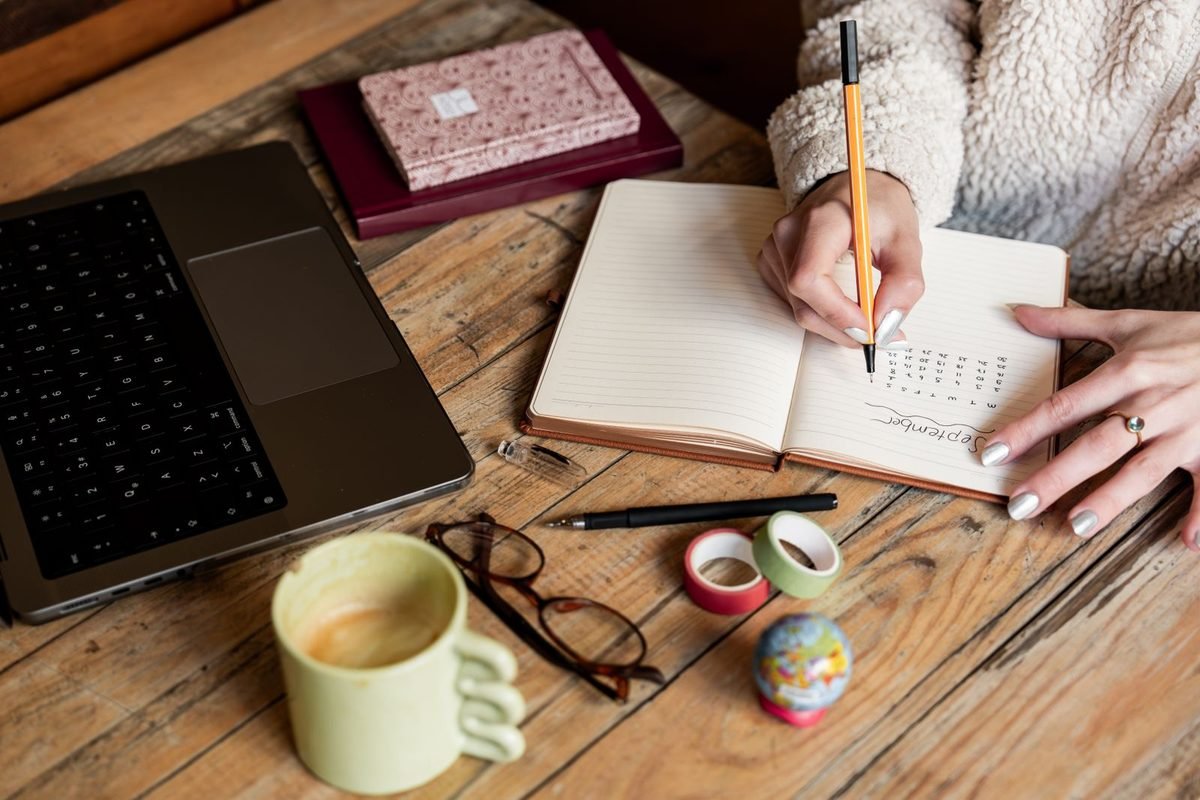 woman planning a schedule in a notebook beside a laptop on a desk