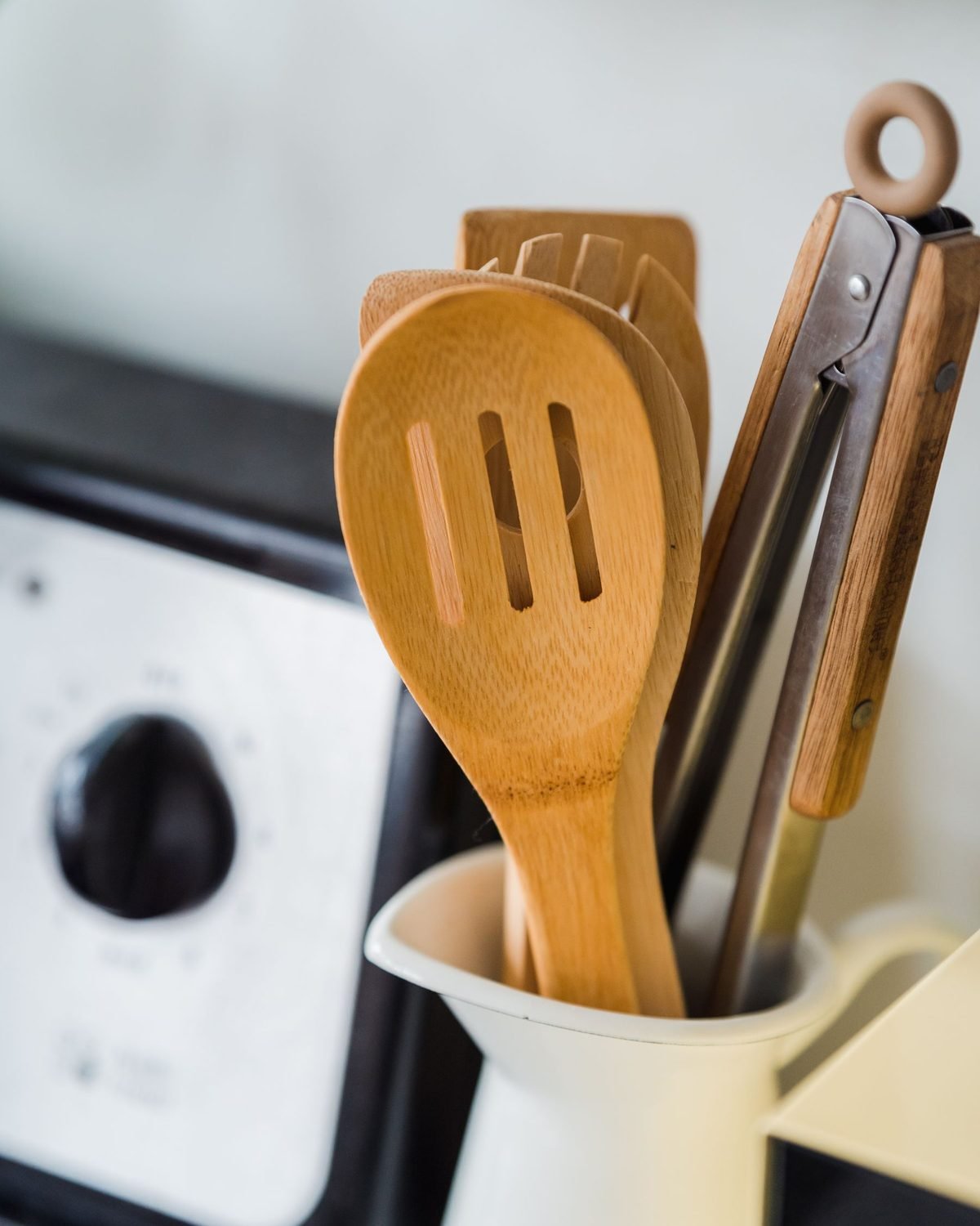 wooden cooking utensils standing in a white crock on a kitchen counter